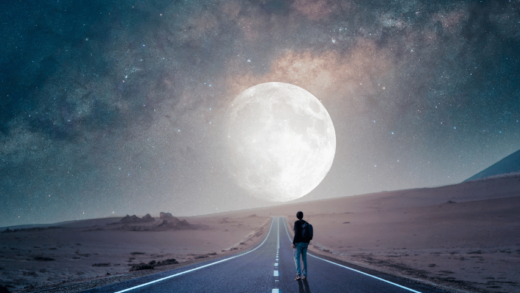 man standing on a deserted street staring at a large moon in the night sky