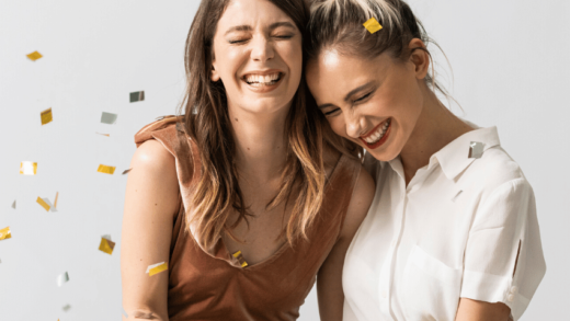 two woman hugging and smiling as gold and silver confetti fly around them