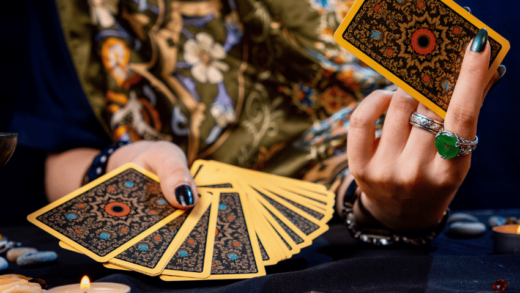 hands adorned with rings holding up gold and black tarot cards