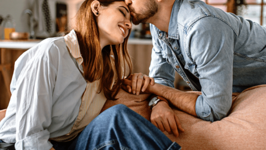 man kissing the forehead of a woman sitting on a couch