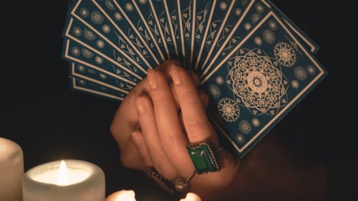 A hand holds a handful of Tarot cards, shown illuminated by candlelight.