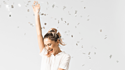 blonde woman in a white shirt and green skirt dancing gleefully with confetti in the air