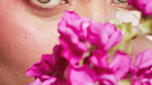 a pair of woman's green eyes, clad with pink eyeshadow, looking over an array of pink flowers