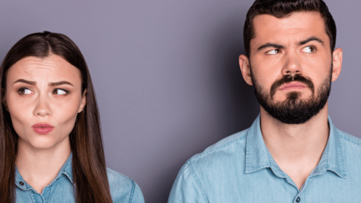 A couple in denim shirts stand next to each other, looking away with consternated expressions on their faces.