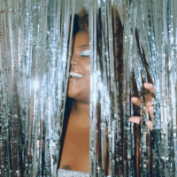 A black woman closes her eyes in pleasure as she enters through a shiny, glittery silver door covering.