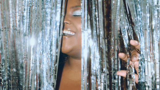 A black woman closes her eyes in pleasure as she enters through a shiny, glittery silver door covering.