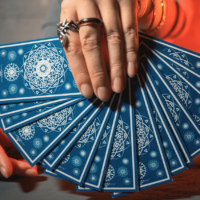 A hand wearing rings holds a fan of blue Tarot cards.